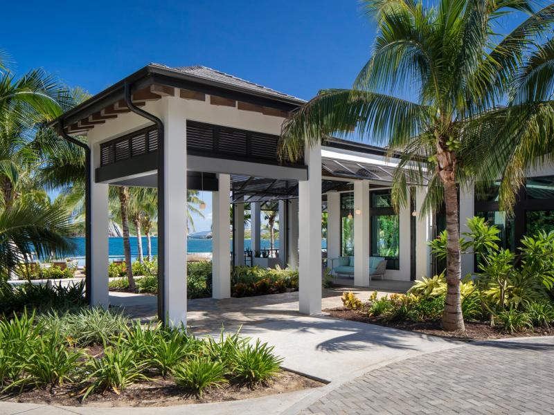 Stylish Peter Island Resort entrance framed by lush green palms and sleek white columns, accented by deep blue skies and charcoal rooflines.