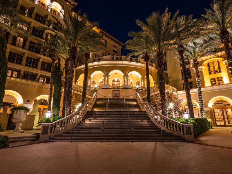 A stunning nighttime view of sweeping the curved staircase leading to gardens and pool framed by towering palms, illuminated with golden arches and soft amber lighting at Green Valley Ranch Resort Spa Casino.