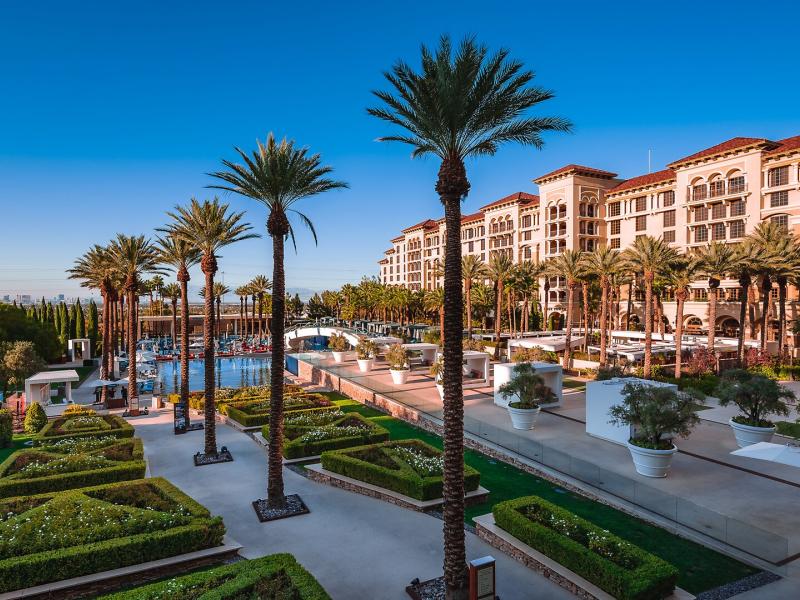 Green Valley Ranch Resort Spa Casino expansive resort grounds with manicured green gardens and sparkling blue pools, complemented by tall palm trees and creamy stone pathways.