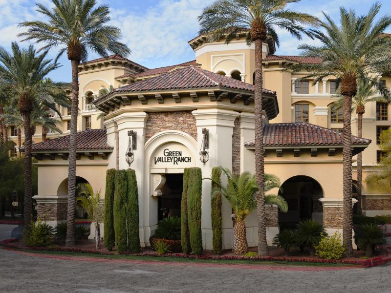 Green Valley Ranch Resort Spa Casino grand Mediterranean-style entrance with elegant stone columns and lush palm trees, accented by warm beige walls and rich terracotta tones.