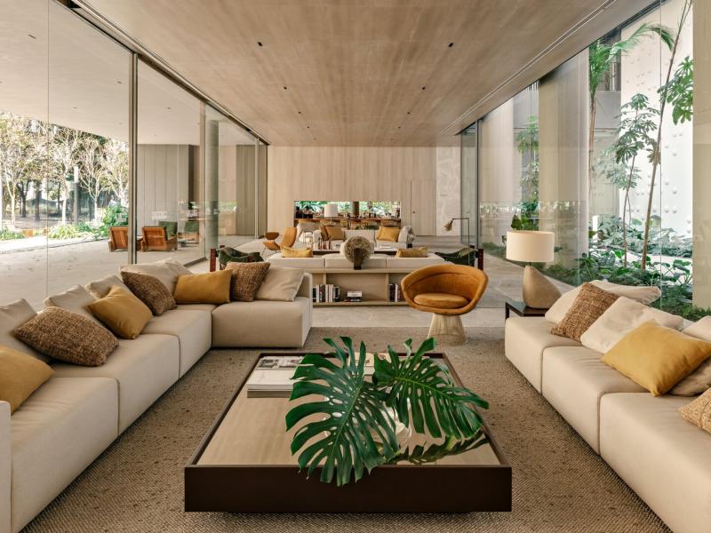 The airy lobby of Pulso Hotel featuring plush ivory seating, golden-hued accent chairs, and panoramic glass walls that open to vibrant greenery for a seamless indoor-outdoor experience.