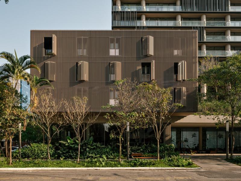 Showcasing a modern architectural design, Pulso Hotel exterior features sleek bronze-toned panels with geometric accents and lush green landscaping framed by tall glass windows.
