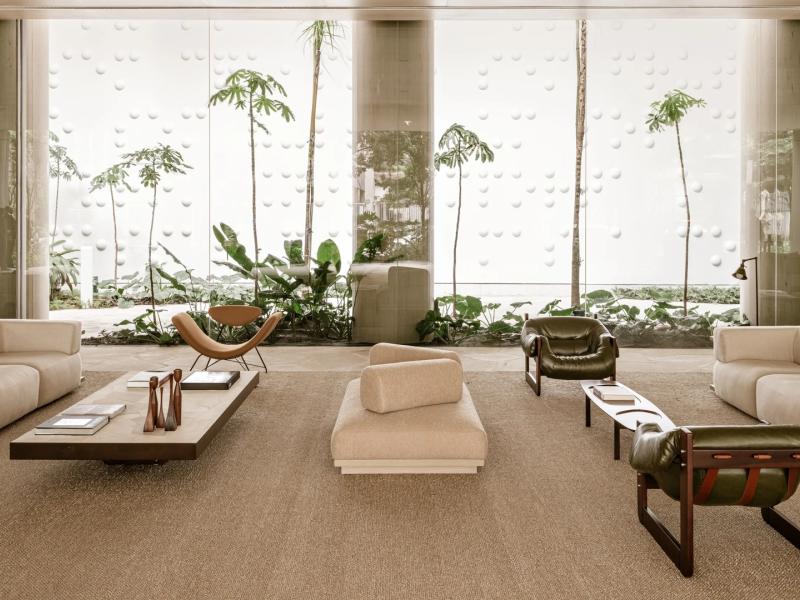 Pulso Hotel tranquil lobby lounge space with sculptural seating in soft beige tones, complemented by deep green accents and a backdrop of soaring glass walls and tropical foliage.