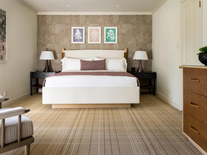 A Premium Suite elegant bedroom featuring a plush white bed with deep brown accents, complemented by textured taupe walls and warm wood tones.