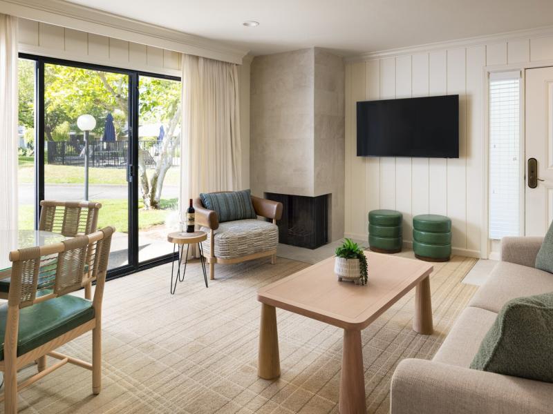 Premium 1 Bedroom Suite with 2 Beds airy living area with floor-to-ceiling windows and a sleek fireplace, accented by soft beige tones and deep green seating.