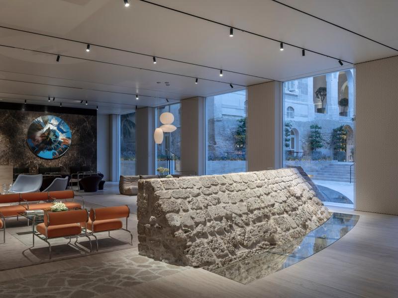 The chic lobby blends historic stone walls with contemporary orange chairs and dark wood accents, highlighted by soft gray flooring.