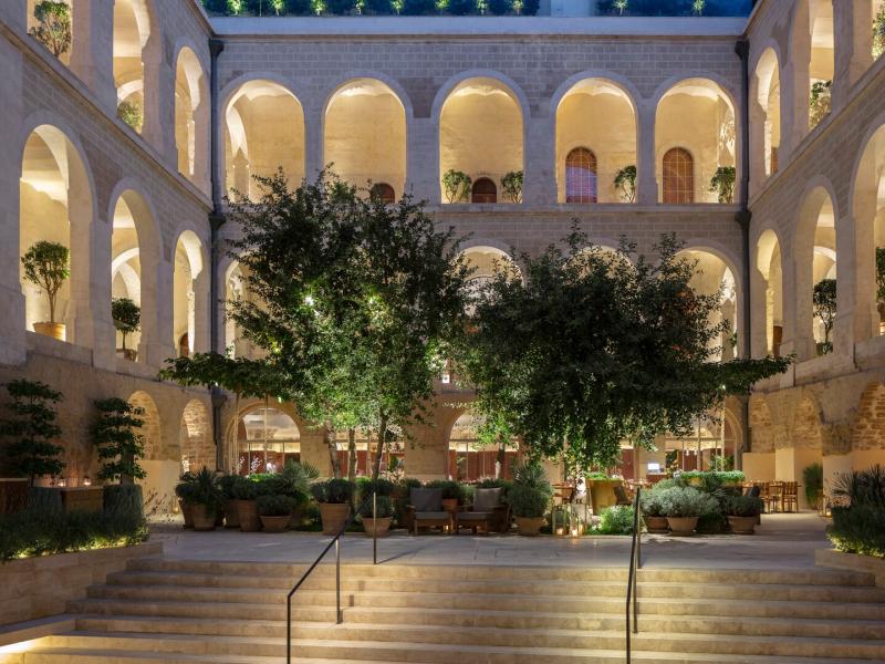 The Jaffa Hotel stunning open-air courtyard framed by elegant stone arches and lush greenery, accented with warm golden lighting and deep green foliage.