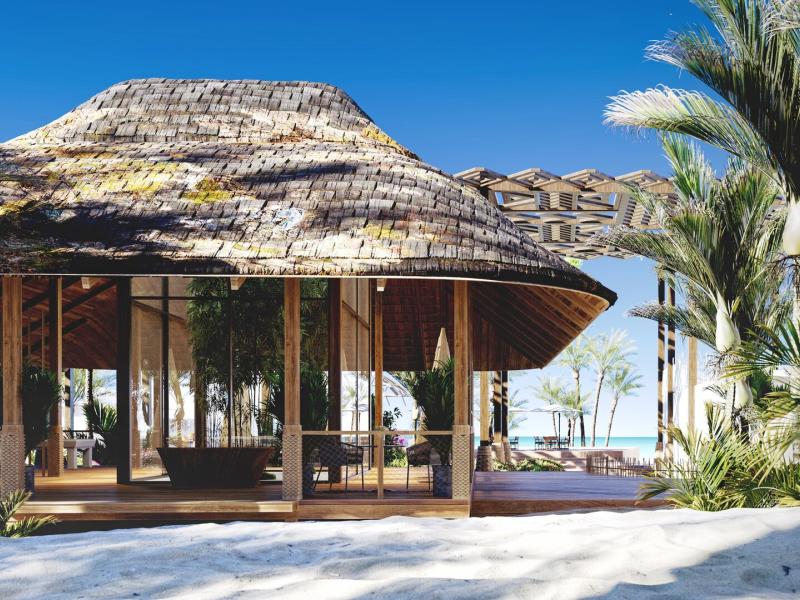ENVI Paje charming beachfront reception pavilion exterior with a rustic thatched roof and natural wood accents, surrounded by lush green palms and pristine white sand under a vibrant blue sky.