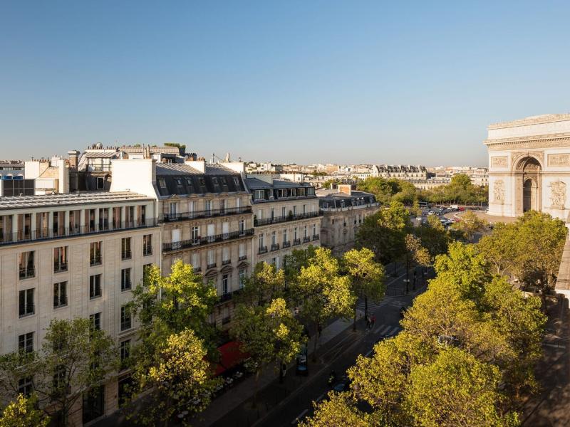 Sweeping views of the Arc de Triomphe and Eiffel Tower framed by elegant white façades and lush green trees under a clear blue sky.