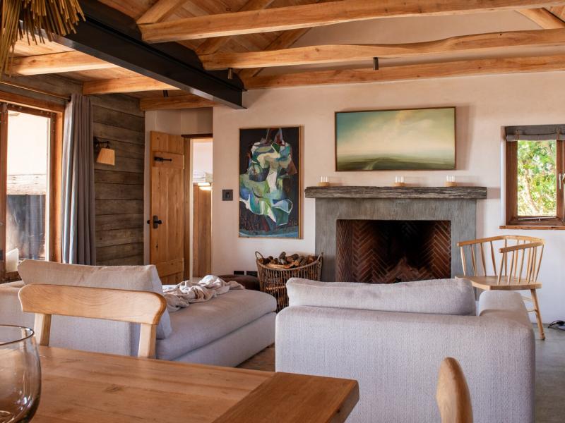 Cozy living space features soft beige sofas, a striking stone fireplace, and natural wood accents, highlighted by calming green artwork.