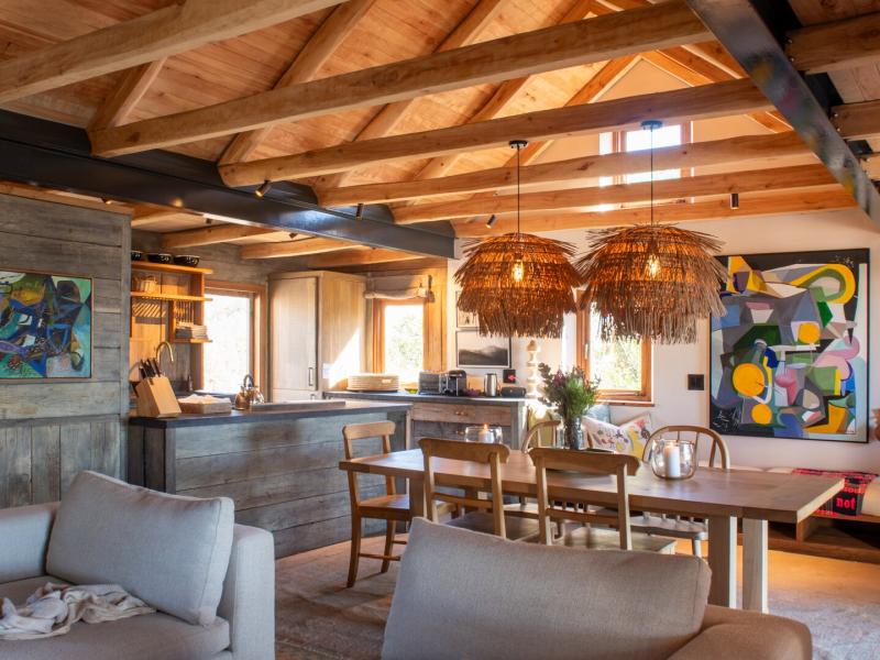 Spacious open-plan dining area shines with warm wood tones and bold pops of yellow and green from abstract art, complemented by rustic woven pendant lights.