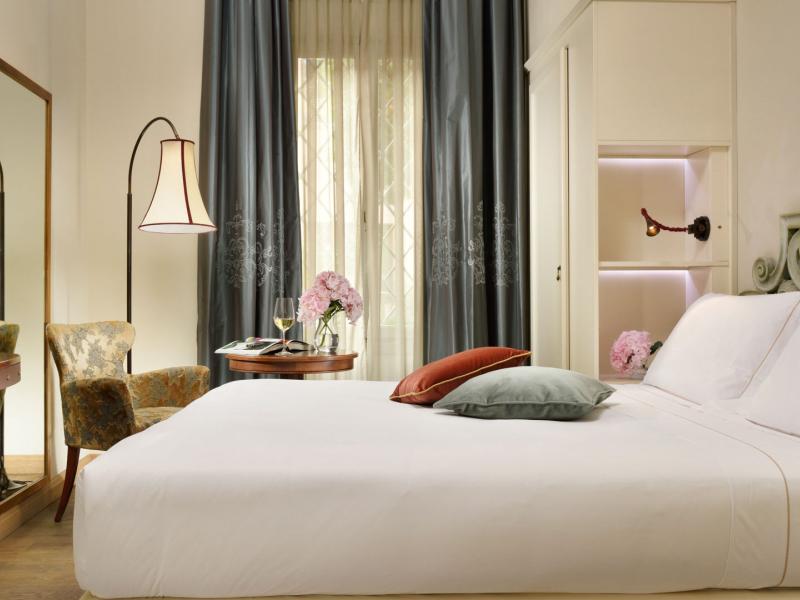 Hotel Ville sull'Arno Villa Superior Double guestroom featuring a plush white bed framed by ornate headboard details, accented with soft gray curtains and pops of earthy green.