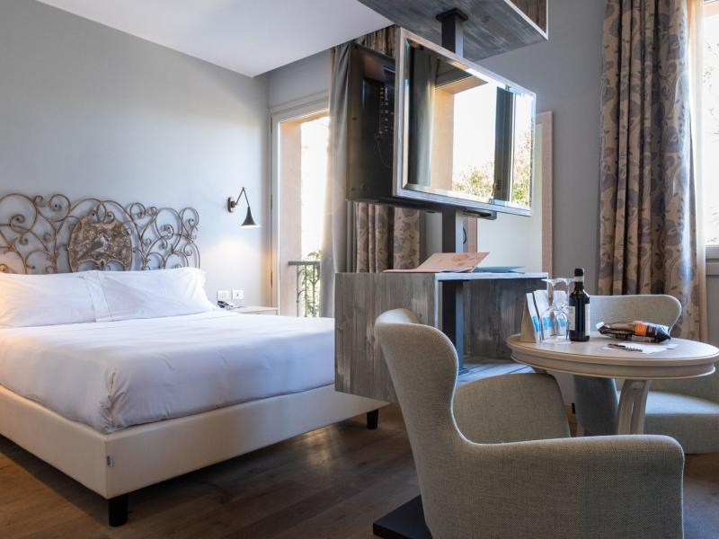 Hotel Ville sull'Arno Superior Double guestroom with elegant wrought-iron headboard and neutral gray tones blend with soft beige accents and natural light, creating a bright, contemporary space.