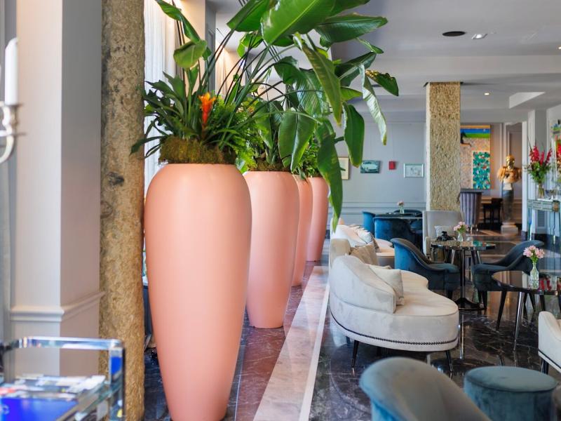 Boscolo Hotel Lyon & Spa airy lobby features plush seating and polished marble floors, brightened by tall peach-colored planters and rich green foliage.