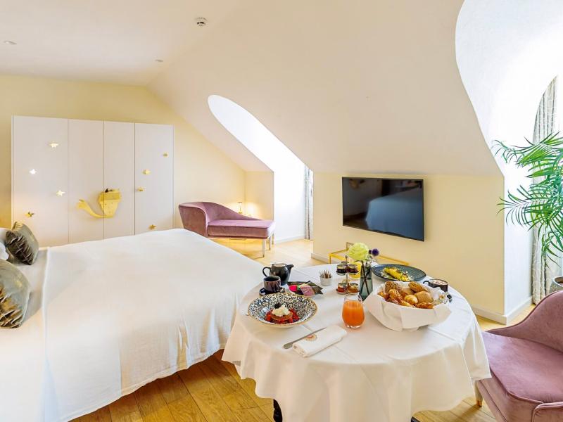 Boscolo Hotel Lyon & Spa Suite featureing a plush white bed and curved architectural windows, accented by soft lavender seating and warm golden décor.