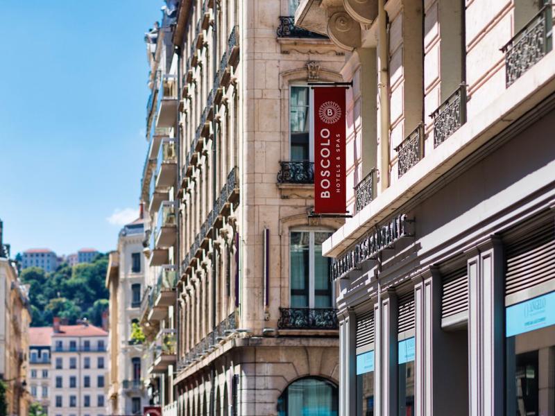 The charming streetside view of Boscolo Hotel Lyon & Spa showcases classic architectural balconies and cream-toned stone, highlighted by it’s bold red vertical sign and touches of sky‑blue detailing.