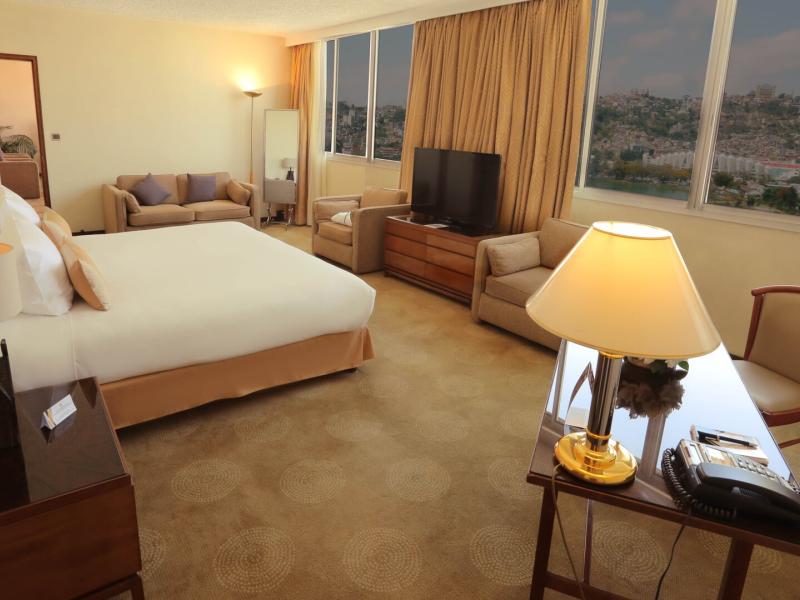 Hotel Carlton spacious Presidential Suite bedroom features a plush king bed and cozy seating area accented with warm beige and soft gold tones.