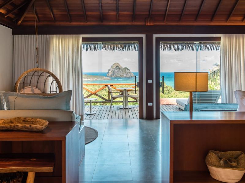 NANNAI Noronha spacious Master Bungalow with elegant wooden accents and soft beige tones, opening to a private deck with stunning turquoise ocean views.