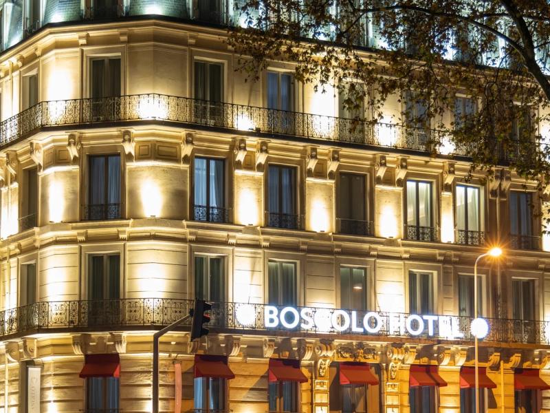 Boscolo Hotel Lyon & Spa grand façade glows with warm golden lighting against elegant cream stonework, accented by deep red awnings and soft blue window reflections.