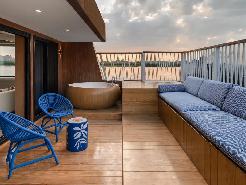 Mazaj Meroot spacious Deluxe Suite deck showcases a smooth wooden floor, a round soaking tub, and plush seating highlighted by vibrant blue and gold accents.