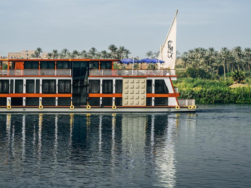 Mazaj Meroot elegant river vessel features sleek modern balconies and crisp geometric paneling accented with warm red and yellow tones against the deep blue water.