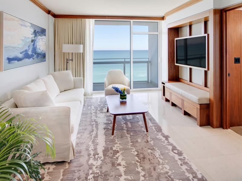 Carillon Miami Wellness Resort spacious oceanfront luxury apartment with warm wood accents, soft cream furnishings, and panoramic views through floor-to-ceiling glass doors.