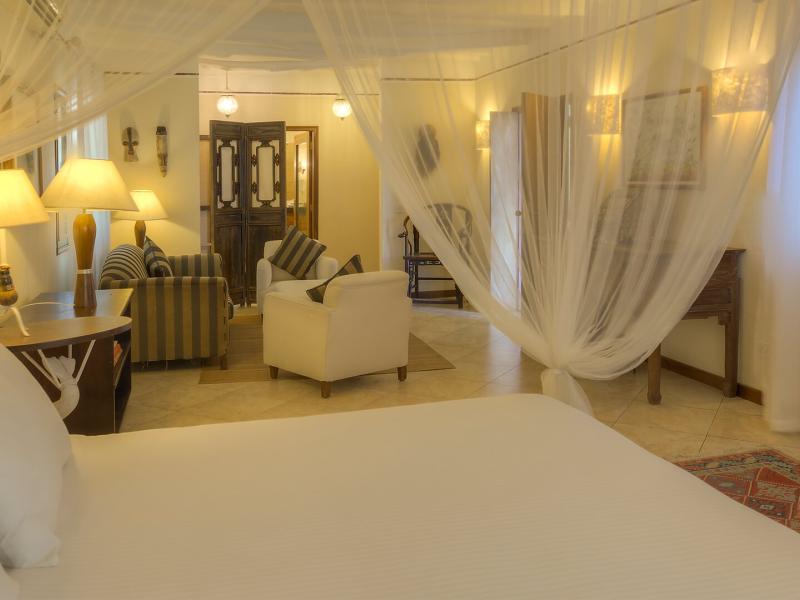 Superior suite bedroom with a white canopy bed, sheer curtains, and warm lighting accented by striped cushions and a patterned area rug.