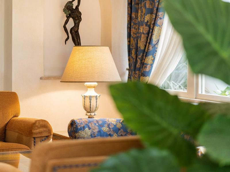 Excelsior Belvedere Hotel & SPA lobby cozy corner adorned with warm tan furnishings and soft lighting, complemented by vibrant greenery and elegant blue floral curtains.