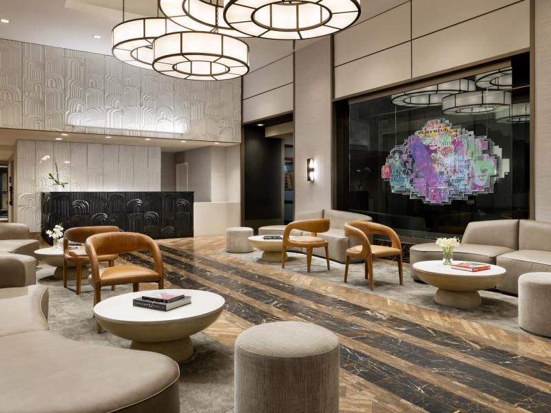 The Muse New York spacious lobby blends creamy beige seating and warm wood tones with striking black marble flooring and a vibrant purple-and-teal art installation.