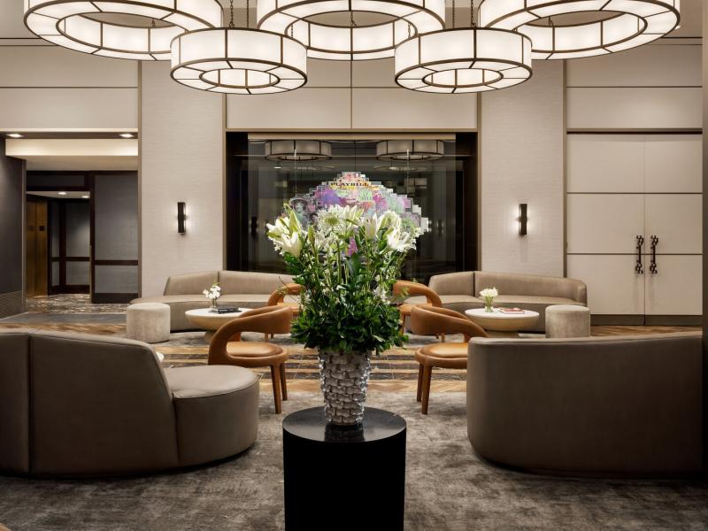 The Muse New York lobby contemporary beige sofas, smooth white tables, and honey‑toned chairs frame a bold multicolored artwork featuring pops of purple and green.