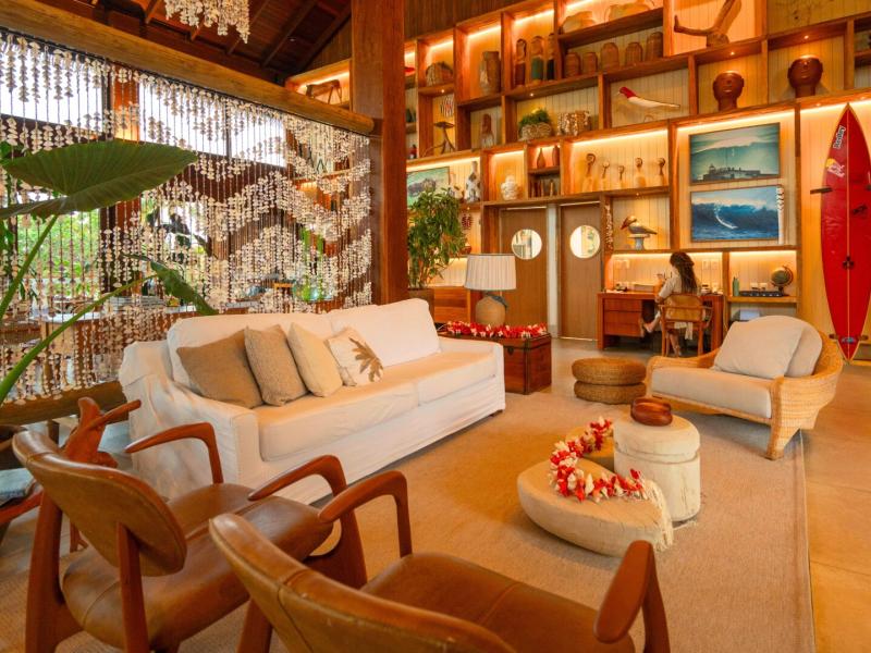 NANNAI Noronha inviting lounge with elegant wooden furniture and soft beige seating, highlighted by vibrant red accents and lush greenery under ambient golden lighting.