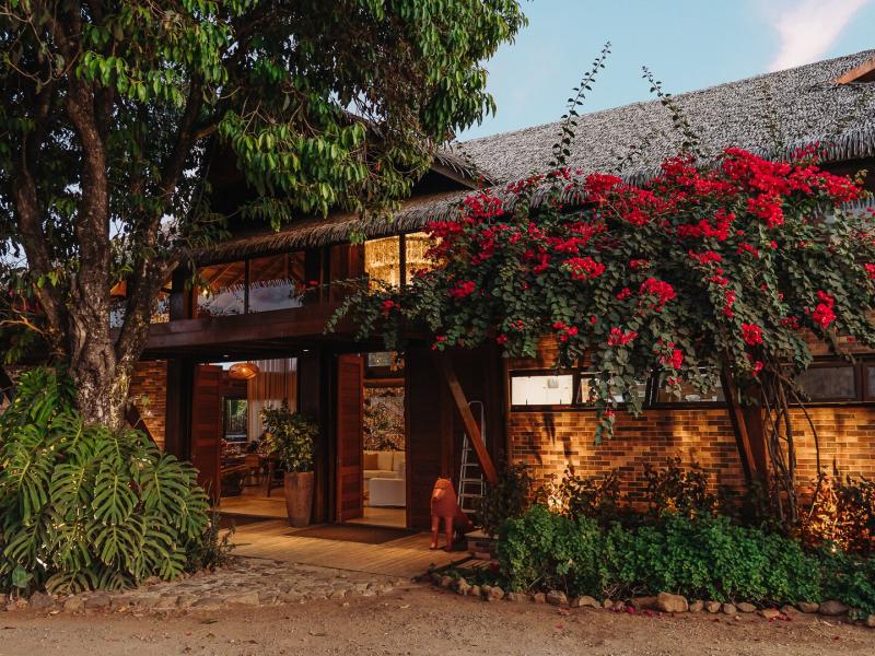 NANNAI Noronha entrance featuring rustic brick architecture and a thatched roof, beautifully accented by vivid red bougainvillea and lush green foliage.