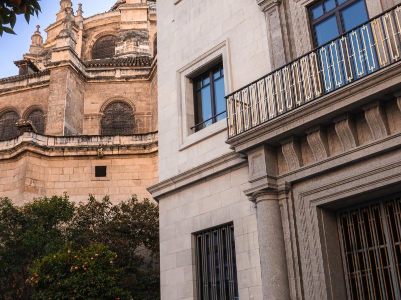 Gran Hotel Claridge Granada elegant stone façade with intricate detailing and warm beige tones accented by deep bronze railings and lush greenery.