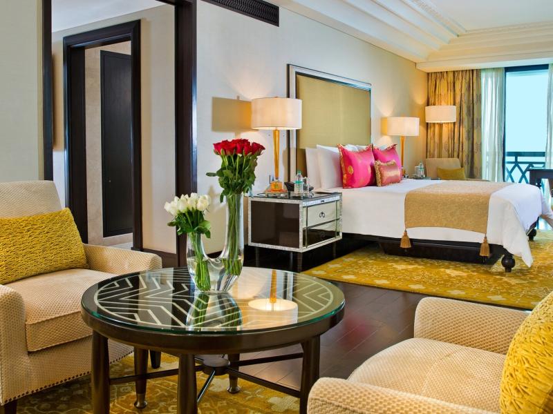 Royal Suite bedroom with modern furnishings, vibrant pink pillows, and warm golden tones complemented by fresh floral arrangements.