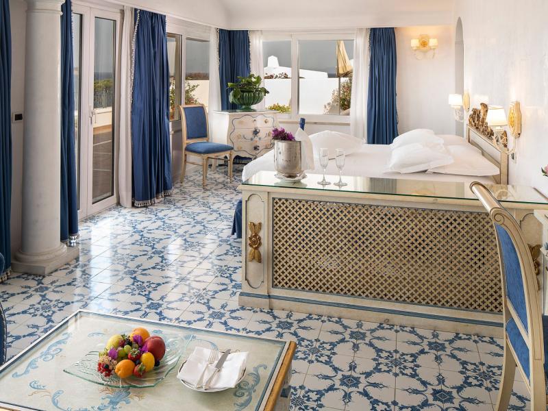 Excelsior Belvedere Hotel & SPA spacious Junior Suite with elegant patterned tile flooring and plush white bedding, accented by rich blue curtains and golden details.
