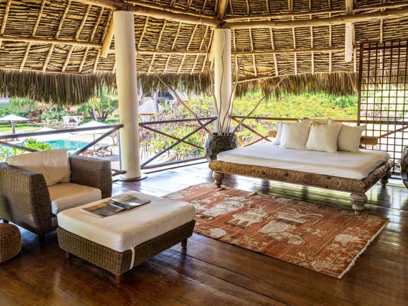 Lion in the Sun Boutique Hotel & Spa veranda lounge with woven rattan furniture, a carved wood daybed, and earthy tones accented by a terracotta rug and vibrant blue ceramic décor.