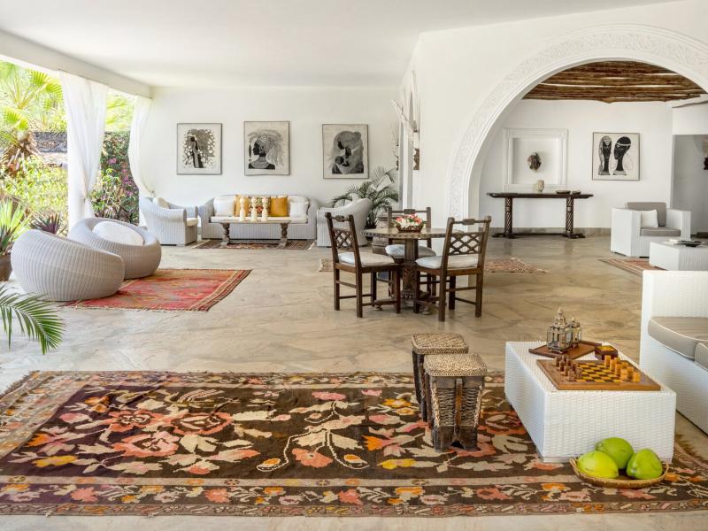 Standard patio featuring crisp white walls, elegant archways, and natural wood furniture accented by bold patterned rugs in warm orange and deep brown.