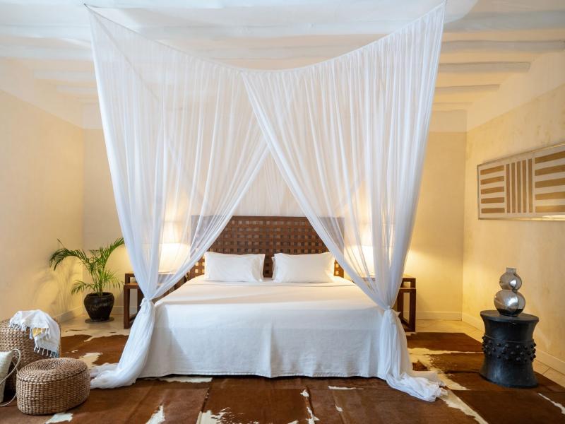 Superior suite bedroom with a flowing white canopy bed, textured wood accents, and earthy tones complemented by soft beige walls and a cowhide rug.