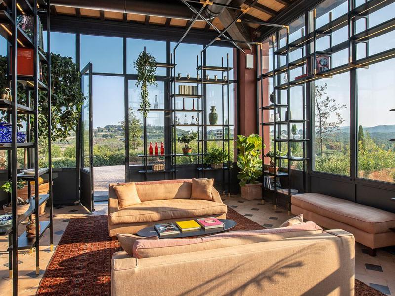 Locanda Rossa’s sun‑filled modern lobby lounge showcases expansive glass walls, cozy contemporary seating, and indoor greenery, accented with warm neutrals, deep blacks, and vibrant natural greens.