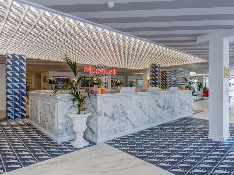 The elegant reception area at Mongibello Ibiza features a marble-front desk, geometric patterned floors, and sculptural lighting, accented in soft white, navy blue, and touches of gold.