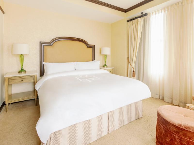 HOTEL DU PONT’s serene One Bedroom Suite sleeping space features a plush king bed and soft draped curtains accented with warm beige and fresh green tones.