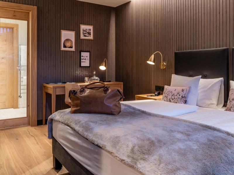 A Superior guest room blends textured dark wood paneling with luxurious gray bedding, accented by soft blush patterns and warm brass lighting.