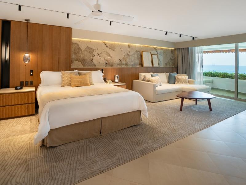 Grand Velas Riviera Nayarit’s elegant Grand Terrace Suite offers a king bed, stylish seating area, and sweeping ocean views, designed with warm wood tones, neutral beiges, and soft blue highlights.