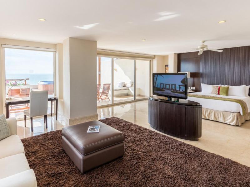 Grand Velas Riviera Nayarit’s bright, open Grand Class Suite with a separate sleeping area, ocean‑view terrace, and contemporary furnishings, highlighted by crisp white, deep brown, and coastal blue accents.