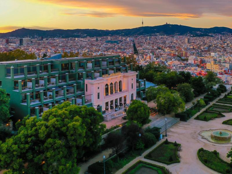 Hotel Miramar sits on a hillside overlooking the Barcelona city skyline, featuring modern green façades, classic architecture, and lush gardens accented by warm sunset hues of gold, blush, and deep emerald.