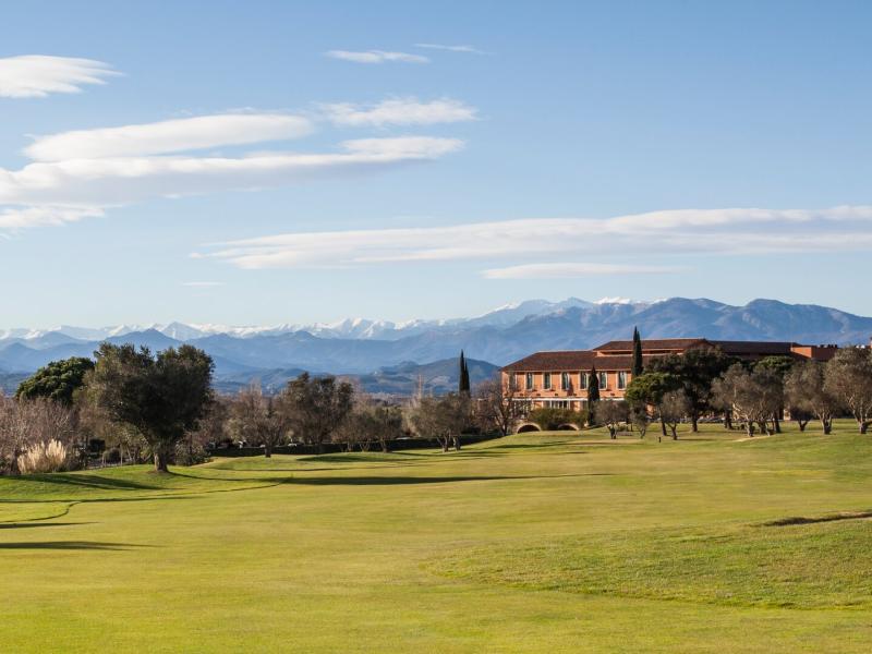 The sweeping green grounds of Hotel Peralada stretches toward its warm terracotta architecture ,accented by the sky’s soft white clouds.