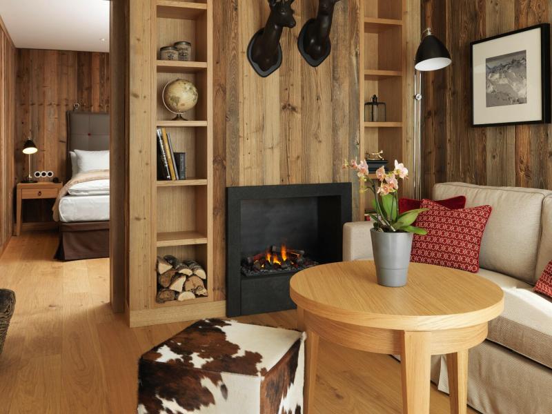 Loewen Hotel Montafon’s charming Hochjoch Suite pairs a snug fireplace and built‑in shelving with cowhide accents and vibrant red cushions for a warm, inviting atmosphere.