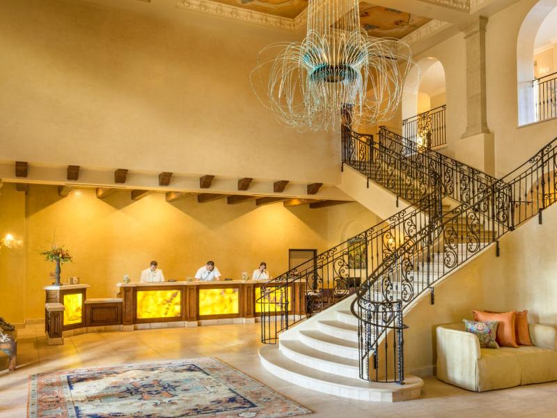 Allegretto Vineyard Resort’s luxurious lobby blends sweeping curved staircases, ornate iron railings, and ambient lighting, complemented by warm gold walls, creamy neutrals, and rich bronze accents.