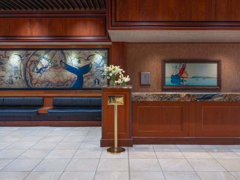 The refined reception space features a polished stone desk, curated artwork, and paneled wood walls, enhanced with creamy neutrals, soft gold fixtures, and subtle blue accents.