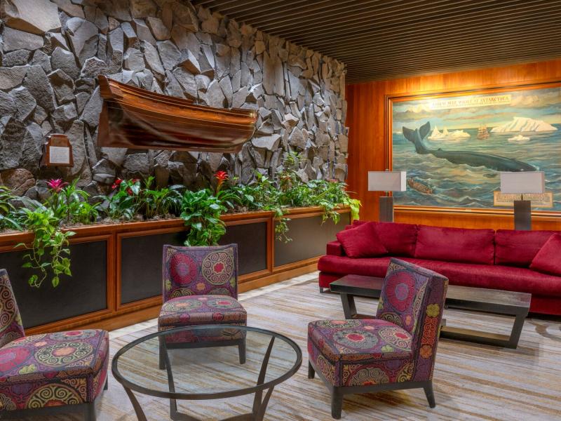 Elegant lobby lounge features a dramatic stone accent wall with sculptural artwork, plush sofas, and layered lighting, highlighted by rich reds, natural stone grays, and warm wood finishes.